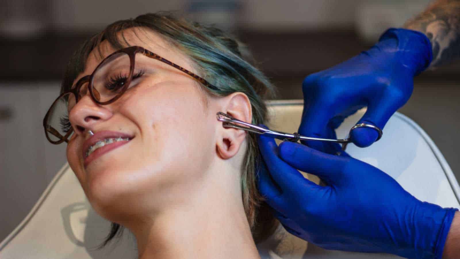 Portrait of a woman getting her ear pierced. Man showing a process of piercing ear . Cleaning the ear and making it steril. Ear Piercing Procedure
